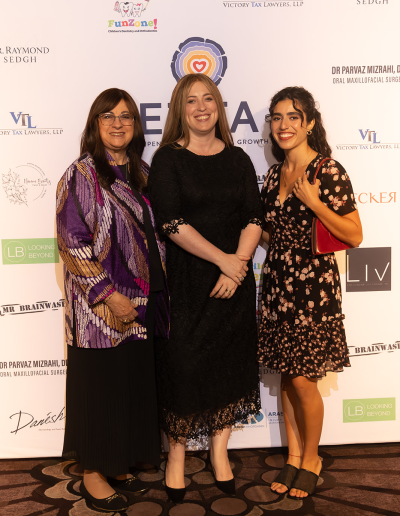 3 women posing in front of the event backdrop.