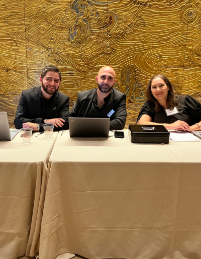 3 people sitting at a table with laptops.